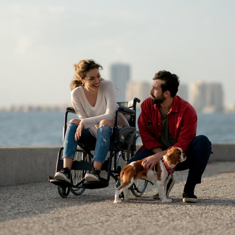 Woman in a wheelchair with a man and a dog by the waterfront